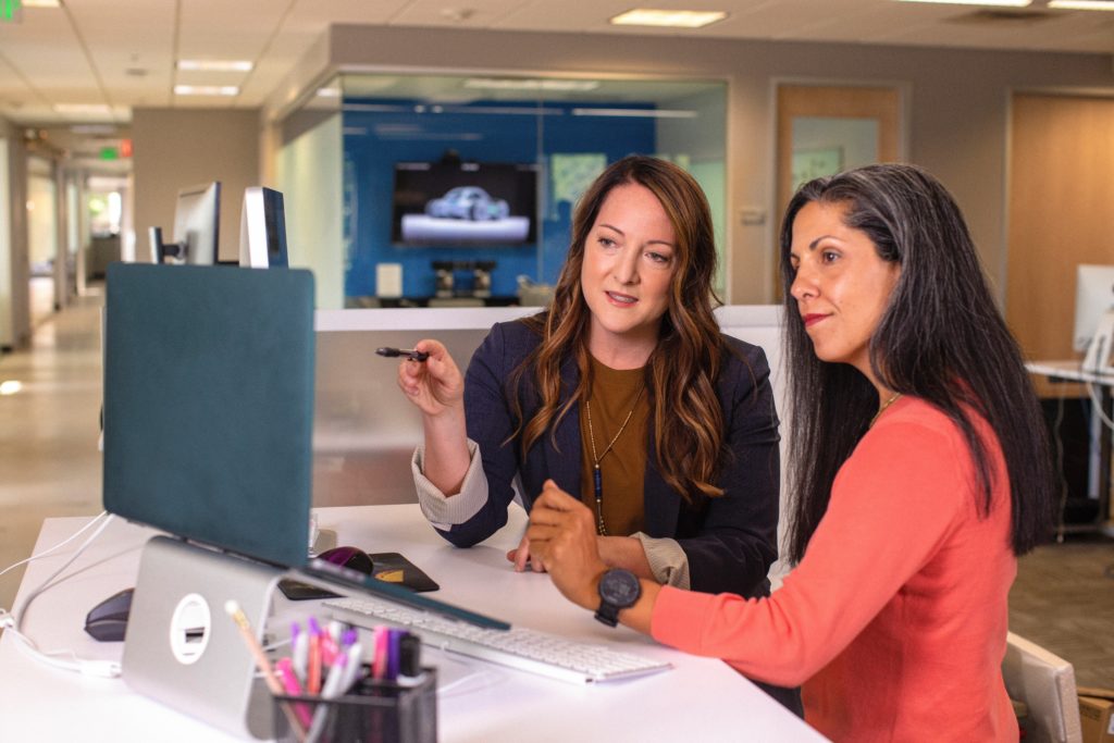 two women sit in front of a computer