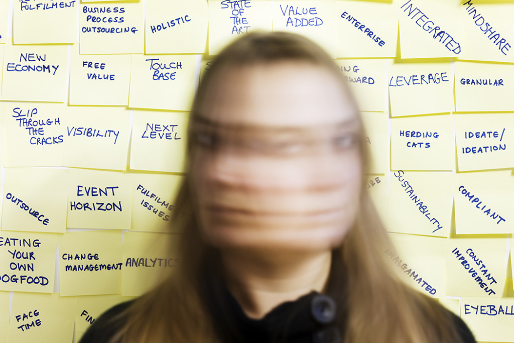 Woman shakes her head in blurred motion as she stands in front of a wall of business buzz words written on yellow sticky notes.